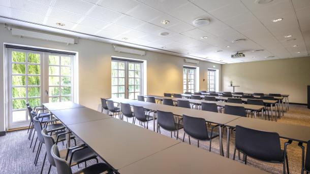 Mødelokale med hvide borde, sorte skalstole og franske vinduer ud til en grøn park