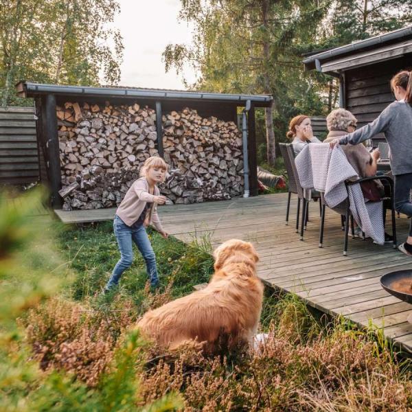 Familie hygger på terrassen i et feriehus i Kystlandet og pige leger med hund og ild i bålfad