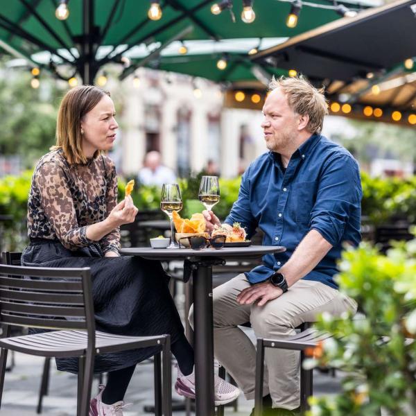 A man and a woman are sitting outside at a bar table under a green parasol