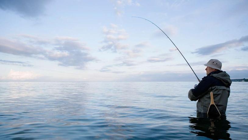 Mand fisker i havet ved solopgang