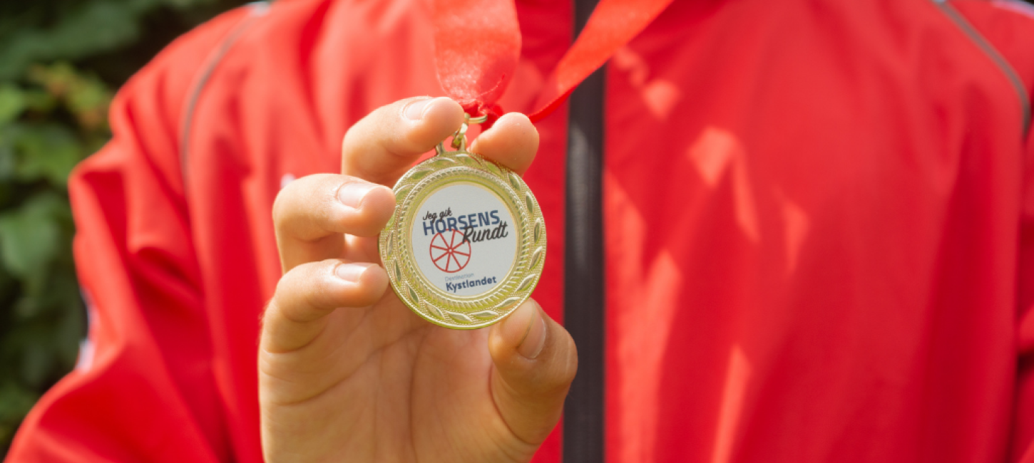 Et barn i rød trøje fremviser Medalje for Horsens Skattejagt 