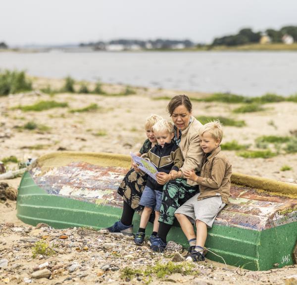 En kvinde sidder med tre små drenge på en strand med et skattekort 